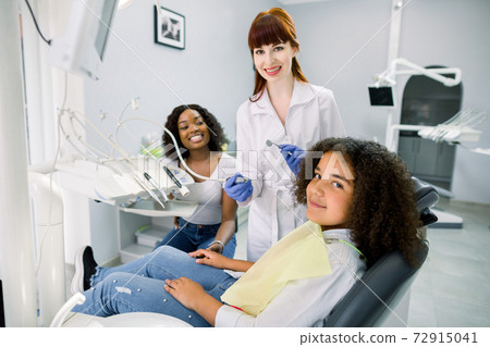 Young smiling African woman mother with her cute preteen daughter, visit their pediatric dentist for regular teeth checkup and treatment at stomatology clinic. Child with mom at dentist's office Young smiling African woman mother with her cute preteen daughter, visit their pediatric dentist for regular teeth checkup and treatment at stomatology clinic. Child with mom at dentist's office 72915041