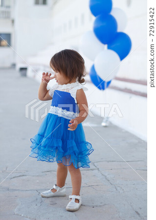 little girl in a beautiful dress with a huge fountain of balloons little girl in a beautiful dress with a huge fountain of balloons 72915422