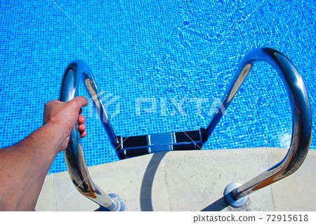 Stairs to the pool filled with clean water. Hand holds the handrail. Stairs to the pool filled with clean water. Hand holds the handrail. 72915618