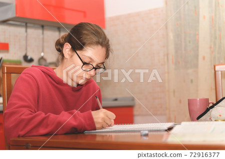 Young student sitting at table in her kitchen and doing her homework, domestic life and distance learning 72916377