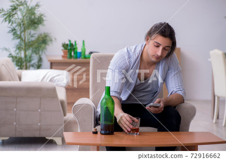 Young male alcoholic watching tv after party 72916662