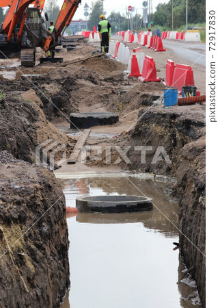 repair work to widen the road. A long ditch filled with sewage with concrete rainwater and excavators in the background. 72917830