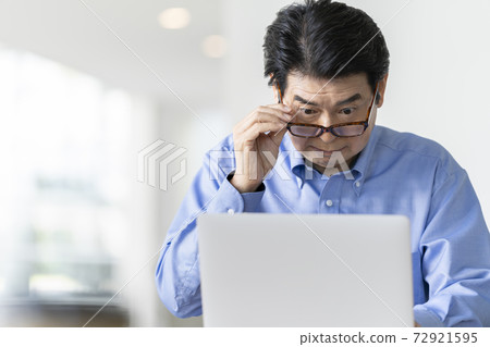 Senior man wearing reading glasses and looking at a laptop screen Senior man wearing reading glasses and looking at a laptop screen 72921595