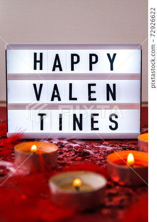 Lightbox with text HAPPY VALENTINES and Burning red candles on confetti sequinned background with feathers. Saint Valentines Day and Christmas background . 72926622