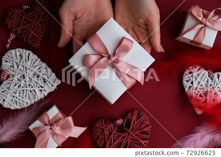 Flat lay of woman hands holding present with box decorated with pink ribbon on red background. Happy valentines day. Christmas Mother's Woman's Day Flat lay of woman hands holding present with box decorated with pink ribbon on red background. Happy valentines day. Christmas Mother's Woman's Day 72926625