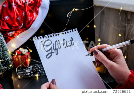 Sheet of paper with text GIFT LIST against Christmas decorations, laptop in Santa hat. Holiday online shopping. Winter sale Sheet of paper with text GIFT LIST against Christmas decorations, laptop in Santa hat. Holiday online shopping. Winter sale 72926631