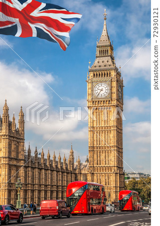 Big Ben with red buses on the bridge against flag of England in London, England, UK 72930121