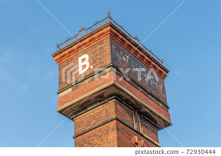 Summer view of red brick water tower against blue sky of the former Battersby Hat Factory, built 1895, Hempshaw Lane, Stockport, UK, now under redevelopment as a housing estate. 72930444