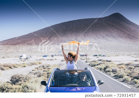 Happiness and travel lifestyle concept with beautiful woman outside a convertible blue car enjoy the freedom and have fun on the road with her female friends driving the vehicle - friends and Happiness and travel lifestyle concept with beautiful woman outside a convertible blue car enjoy the freedom and have fun on the road with her female friends driving the vehicle - friends and 72931457