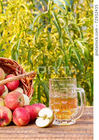 Just picked apples in a wicker basket and apple cider in glass goblet 72932435