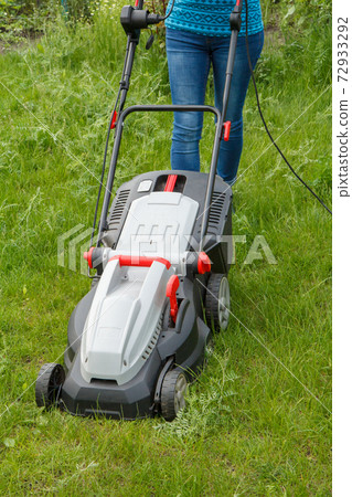 Woman is operating with lawn mower in the garden Woman is operating with lawn mower in the garden 72933292