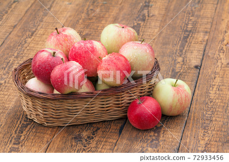 Red apples in wicker basket on wooden boards 72933456