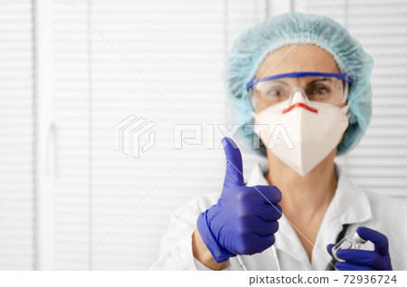 Portrait of happy smiling caucasian female doctor in mask glasses gloves and hat shows thumb up on white window background 72936724