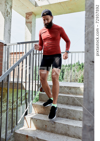 Concentrated male athlete running up stairs to make training more intensive. Sporty handsome young man training alone outdoors. Staircase workout concept 72937892