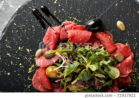 Beef carpaccio with arugula on a black plate, traditional Italian cuisine. Dark key, copy space, Beef carpaccio with arugula on a black plate, traditional Italian cuisine. Dark key, copy space, 72937922