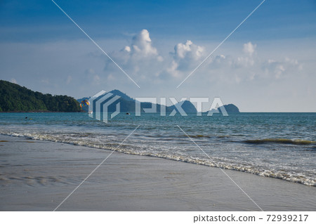 Waves of the azure Andaman sea under the blue sky reaching the shores of the sandy beautiful exotic and stunning Cenang beach in Langkawi island 72939217