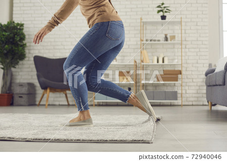 Clumsy woman trips over the rug in the living-room and is about to fall on the floor Clumsy woman trips over the rug in the living-room and is about to fall on the floor 72940046