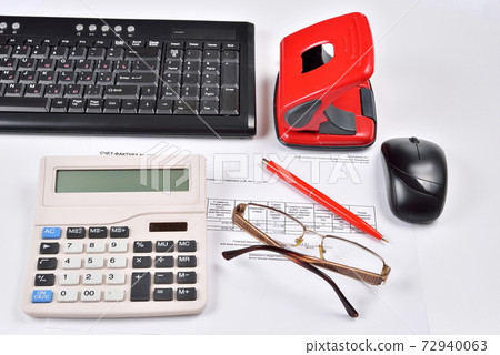 On the Desk of the accountant: invoice, keyboard, calculator, mouse, hole punch, glasses and red pen 72940063