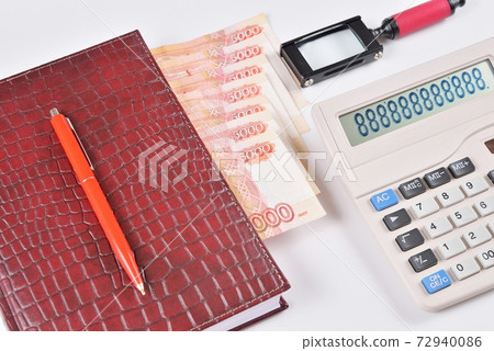 Close-up: business diary with bookmark and pen lying next to a calculator and a magnifying glass 72940086