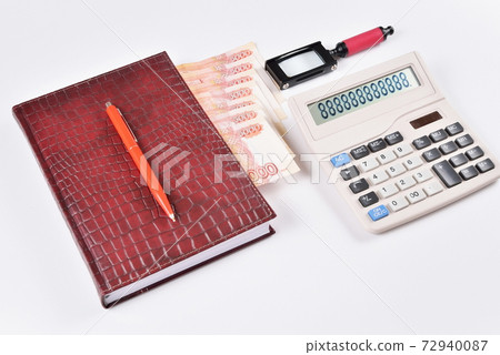 Business diary with bookmark and pen lying next to a calculator and a magnifying glass 72940087