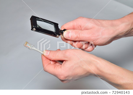 Hands of the installer Ethernet hold the magnifying glass and cable 72940143