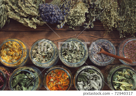 Jars of dry medicinal herbs - calendula, melissa, wild marjoram, lavender, heather, coneflowers, raspberry and currant leaves, linden tree flowers and bunches of herbs. Top view. Jars of dry medicinal herbs - calendula, melissa, wild marjoram, lavender, heather, coneflowers, raspberry and currant leaves, linden tree flowers and bunches of herbs. Top view. 72940317