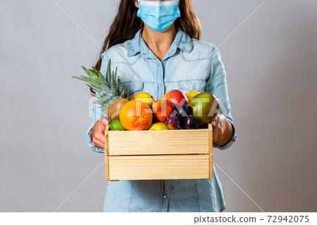 Brunette woman with surgical mask delivering box filled with fruit 72942075