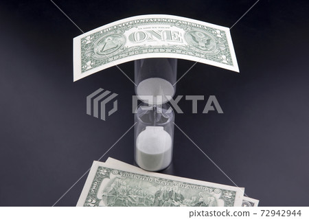 Dollar bills lie near the hourglass. Time is money. The salary. Business solutions in time. 72942944