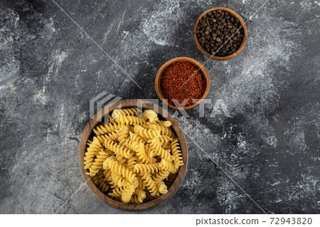 Raw fusilli pasta in wooden bowl with pepper spices 72943820