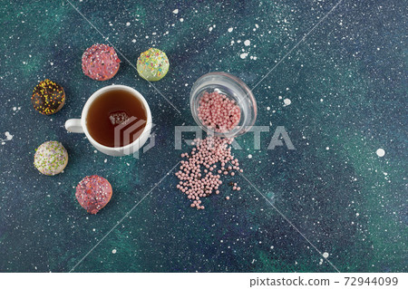 A white cup of tea with small delicious doughnuts 72944099