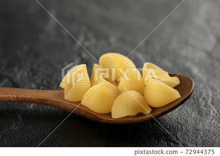 A wooden spoon of uncooked conchiglie macaroni 72944375