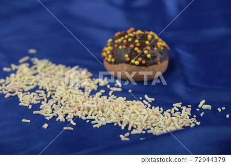 A chocolate small doughnut with sprinkles on a blue tablecloth A chocolate small doughnut with sprinkles on a blue tablecloth 72944379
