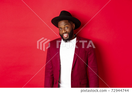 Christmas shopping and people concept. Handsome bearded african american guy looking at camera, smiling confident, wearing party clothes, red background 72944744