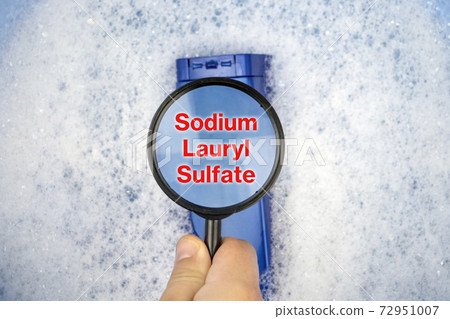 Chemical components on the shampoo label:  Sodium Lauryl Sulfate (sls, sles). A hand holds a blue jar and a magnifier, where the harmful ingredients of a detergent are written in close up. 72951007