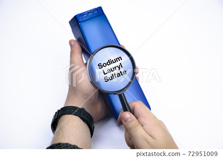 Chemical components on the shampoo label:  Sodium Lauryl Sulfate (sls, sles). A hand holds a blue jar and a magnifier, where the harmful ingredients of a detergent are written in close up. 72951009