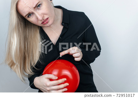 Conceptual photography. The woman holds a red ball near his belly, which symbolizes bloating and flatulence. Then she brings a needle to it to burst the balloon and thus get rid of the problem. Conceptual photography. The woman holds a red ball near his belly, which symbolizes bloating and flatulence. Then she brings a needle to it to burst the balloon and thus get rid of the problem. 72951017