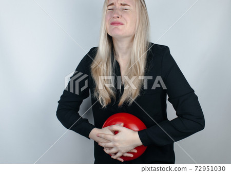 Bloating and flatulence concept. The woman holds a red balloon near the abdomen, which symbolizes bloating. Intestinal tract and digestive system. Problems with flatulence and gastrointestinal tract 72951030