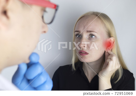A woman suffers from pain in the ear. The auditory meatus hurts due to otitis media, cerumen plug, ear boil, or trigeminal neuralgia. On examination by a doctor. 72951069