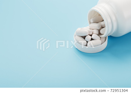 White capsules with vitamins and minerals in the form are poured from a jar on a blue background. 72951304