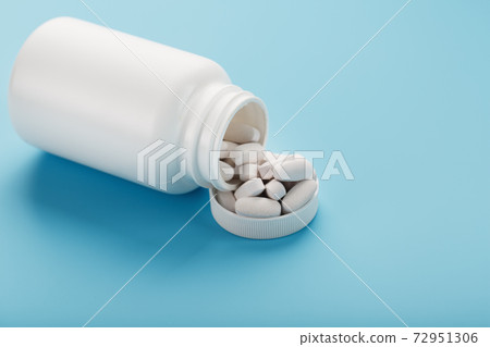 Vitamins and minerals in white capsules fell out of a white jar on a blue background. 72951306