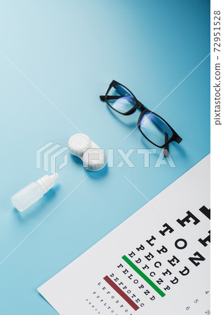 Glasses with Contact Lenses, drops and an Optometrist's Eye Test Chart On a Blue Background. Glasses with Contact Lenses, drops and an Optometrist's Eye Test Chart On a Blue Background. 72951528