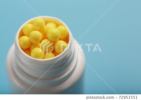 Vitamins of yellow color in the form of round dragees in a white jar on a blue background. Vitamins of yellow color in the form of round dragees in a white jar on a blue background. 72951551
