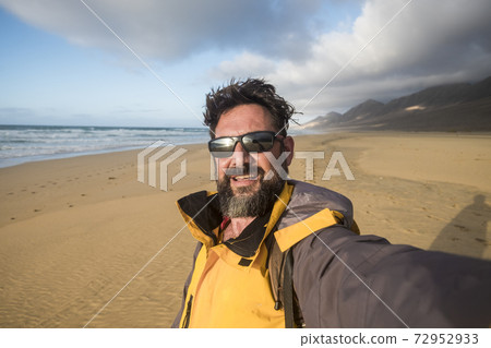 Happy wild lifestyle people concept with cheerful handsome adult man in wild beach with mopuntains in background - alternative summer vacation with adventure taste - caucasian male selfie 72952933