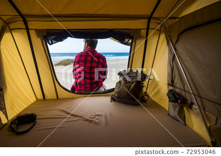 Tent free camping wild lifestyle for alternative vacation inside view and man sitting on the door enjoying the feeling and the free scenic place - backpack and travel people lifestyle - ocean and 72953046