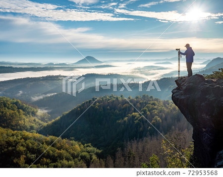 Photographer in silhouette carrying tripod with big camera 72953568