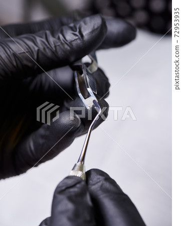 Macro shooting of orthodontic ceramic bracket in dentist's hands wearing black latex gloves. 72953935