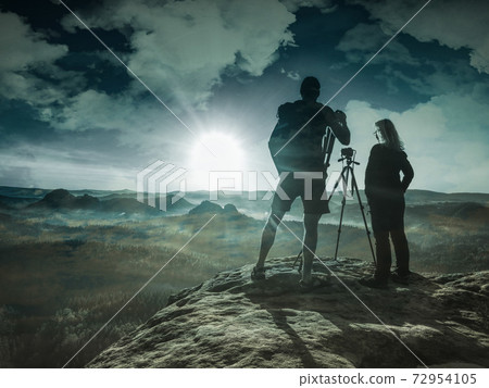 Rear view of couple photographers standing together with cameras and tripod Rear view of couple photographers standing together with cameras and tripod 72954105
