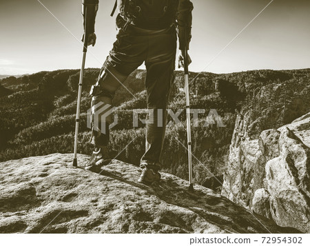 Disabled young man walking on two crutches in landscape. 72954302