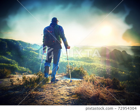 Man with a leg injury leaning on forearm crutches is standing by cliff e 72954304