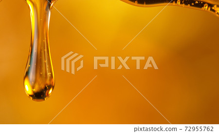 Pouring oil or honey drop on golden background. 72955762